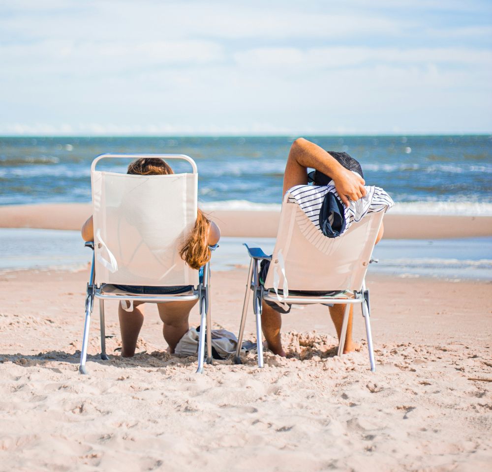 two people sitting on deck chairs on a beach