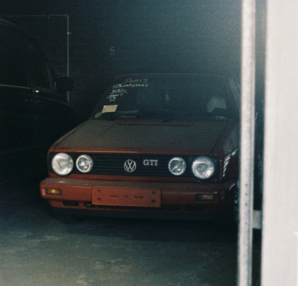 A red Volkswagen GTI is parked in a dimly lit garage, partially obscured by a white doorframe. Writing is visible on the windscreen, and with no number plate on the front, SORN insurance could be ideal for this stored vehicle.