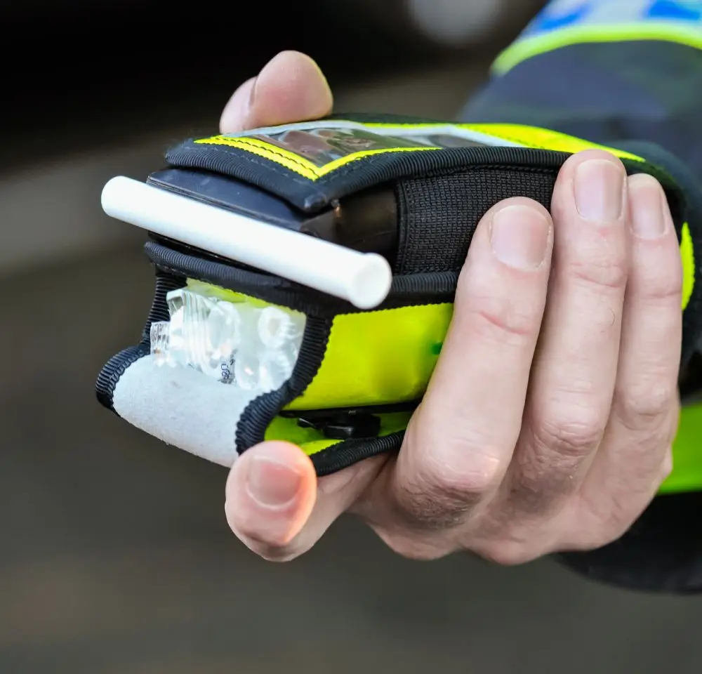 A close-up of a person holding a portable breathalyser device with a white mouthpiece, used for measuring blood alcohol levels—a crucial tool for those concerned about avoiding a DR20 driving conviction. The person is wearing a yellow and black garment.