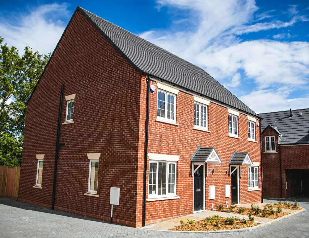 A modern semi-detached red brick house with white-framed windows and two front doors, set against a blue sky with scattered clouds. Ideal for landlords, it’s perfect for those seeking HMO Landlord Insurance or standard Landlord Insurance.