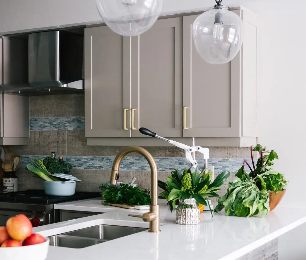 Modern kitchen with light grey cabinets, a gold tap, and a white worktop. Fresh leafy vegetables and apples sit on the counter—a beautiful space that deserves the protection of Property Owner Insurance for peace of mind.