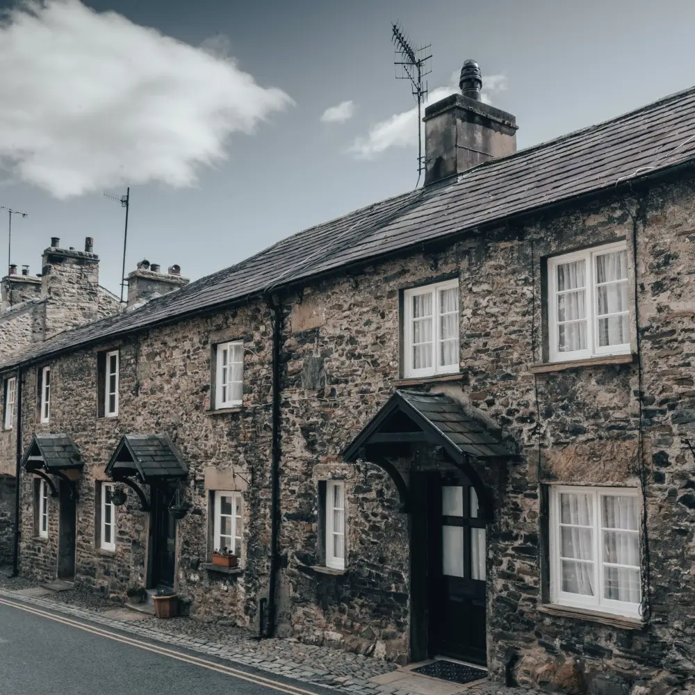 A row of old stone terraced houses with white-framed windows and wooden door canopies, lining a narrow, quiet street under a cloudy sky—perfect for owners seeking landlord insurance peace of mind.