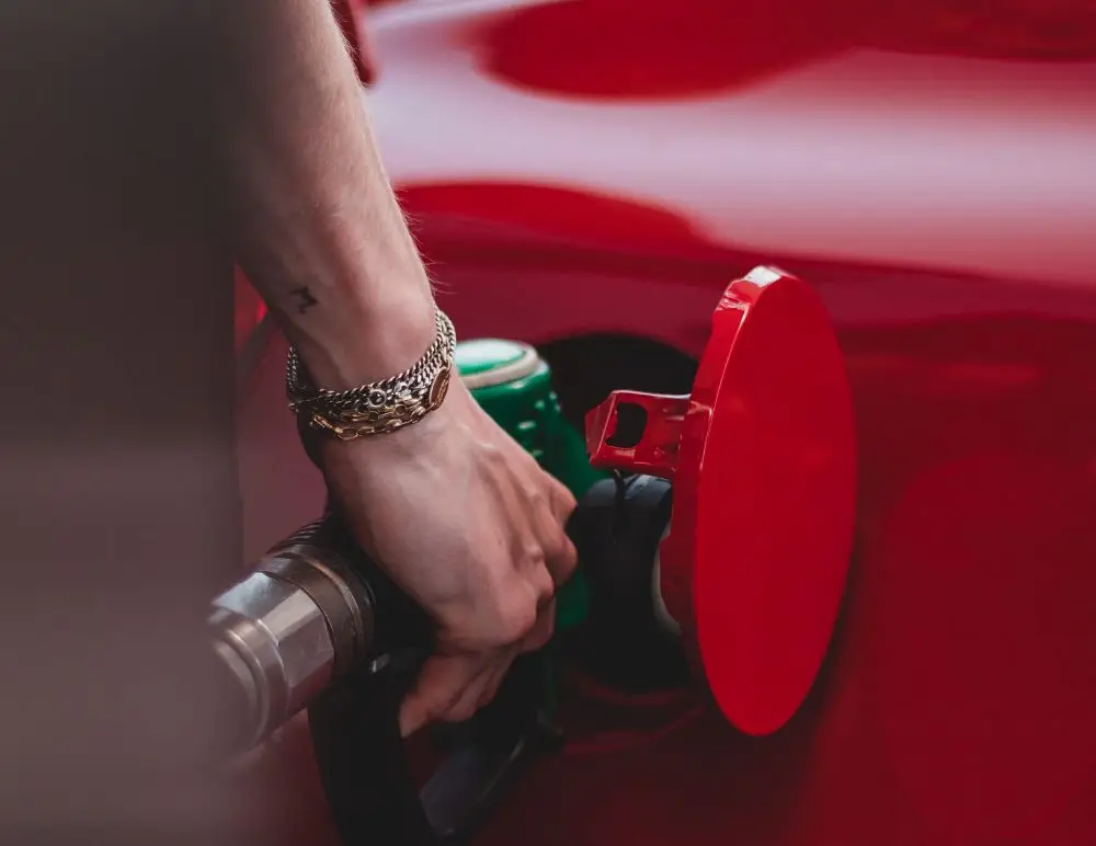 A close-up of a person's hand wearing a bracelet, holding a green fuel nozzle while filling up a red car at a petrol station—perfect for illustrating the importance of Private Misfuelling Cover.