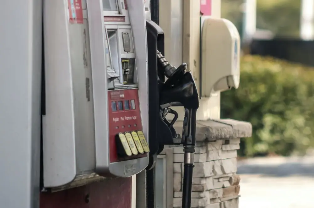 Close-up of a petrol pump at a petrol station, nozzle resting on its holder. The background features a stone column and blurred greenery—reminding you that misfuelling insurance cover can help protect your refuelling experience.