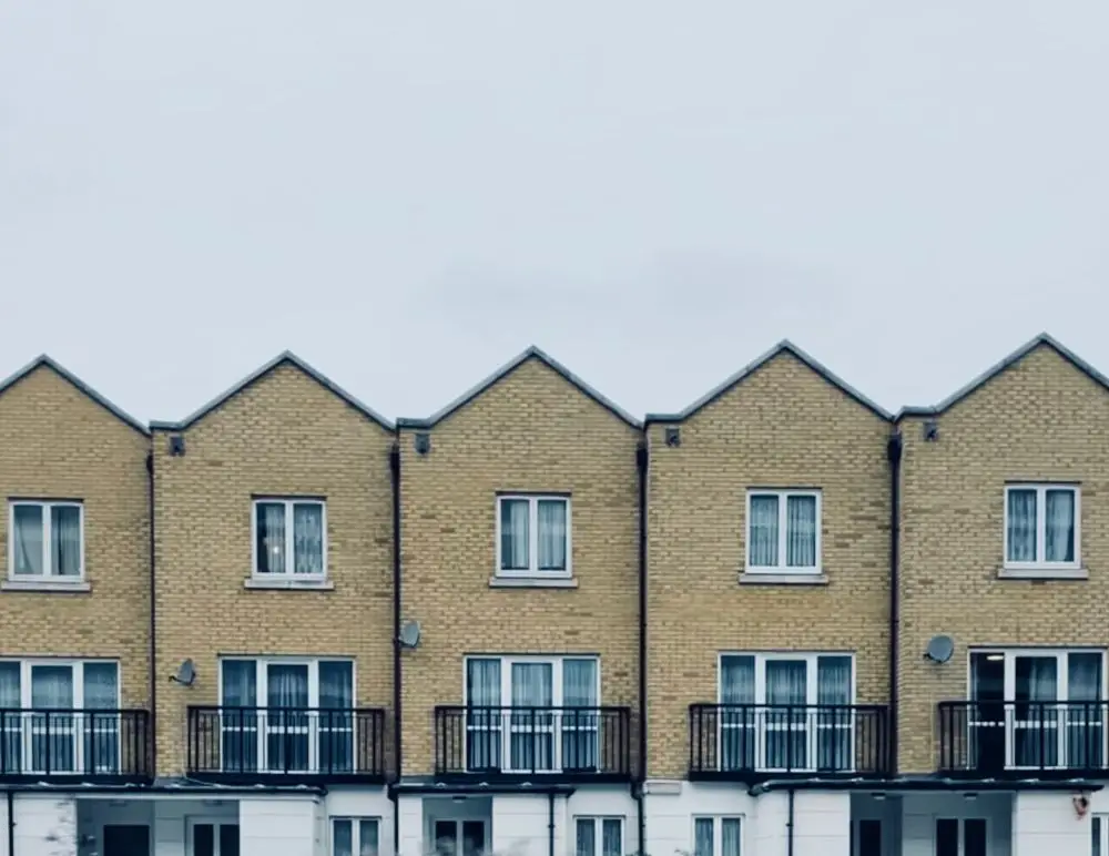 A row of modern, yellow-brick terraced houses with triangular roofs, white-framed windows, and black metal balconies stands out under a pale, overcast sky—ideal properties for those seeking HMO landlord insurance.