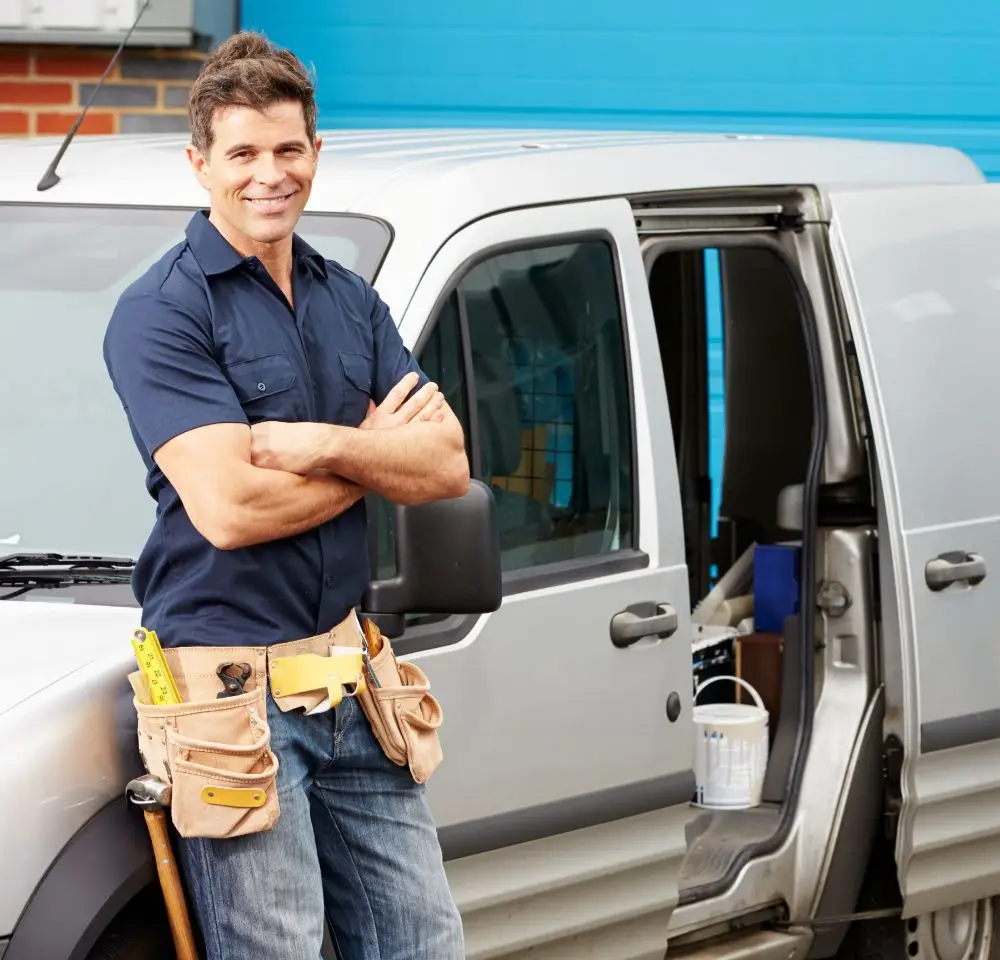 tradesman leaning again silver van with side door open revealing tools inside